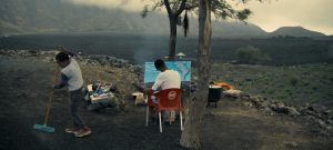 Two children in a hazy landscape. One is seated at an easel. One is pushing a broom.