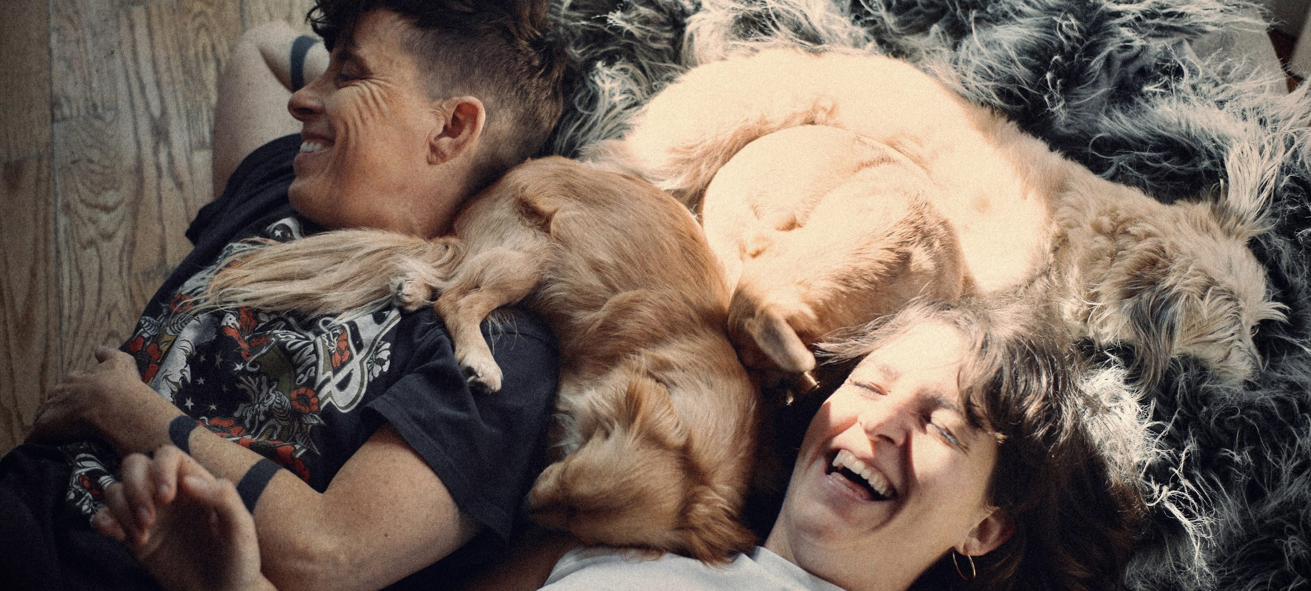 Two smiling people relax on the floor with their dogs.