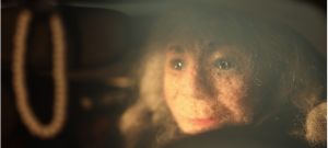 A felted puppet head looks out over a car steering wheel.