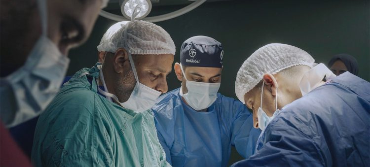 Doctors in masks and scrubs look down at the operating table